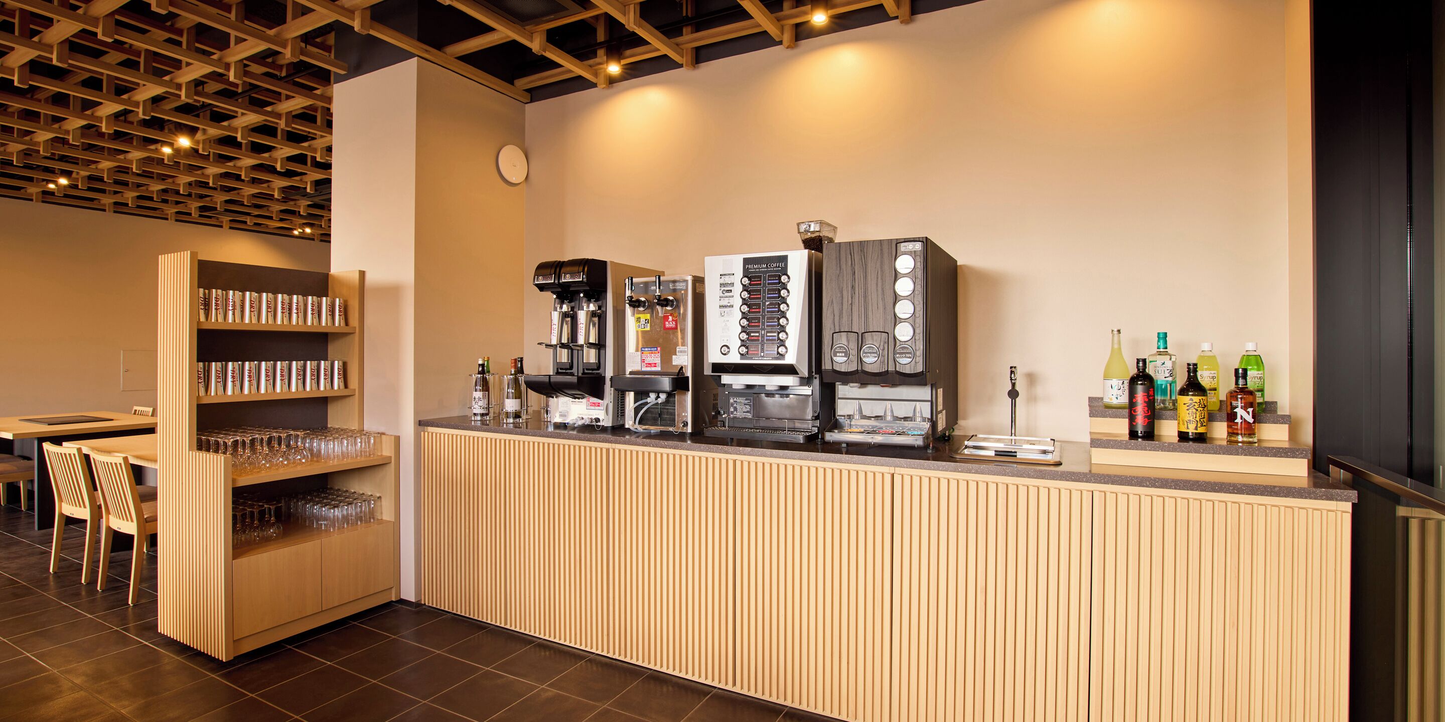 Una zona de bar moderna con mostrador de madera, varias máquinas de café y una selección de botellas.