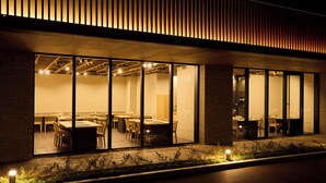 A modern building exterior at night with large glass windows, a brick facade, and a wooden slatted roof. - Rakuten STAY Awara Onsen (Awara)