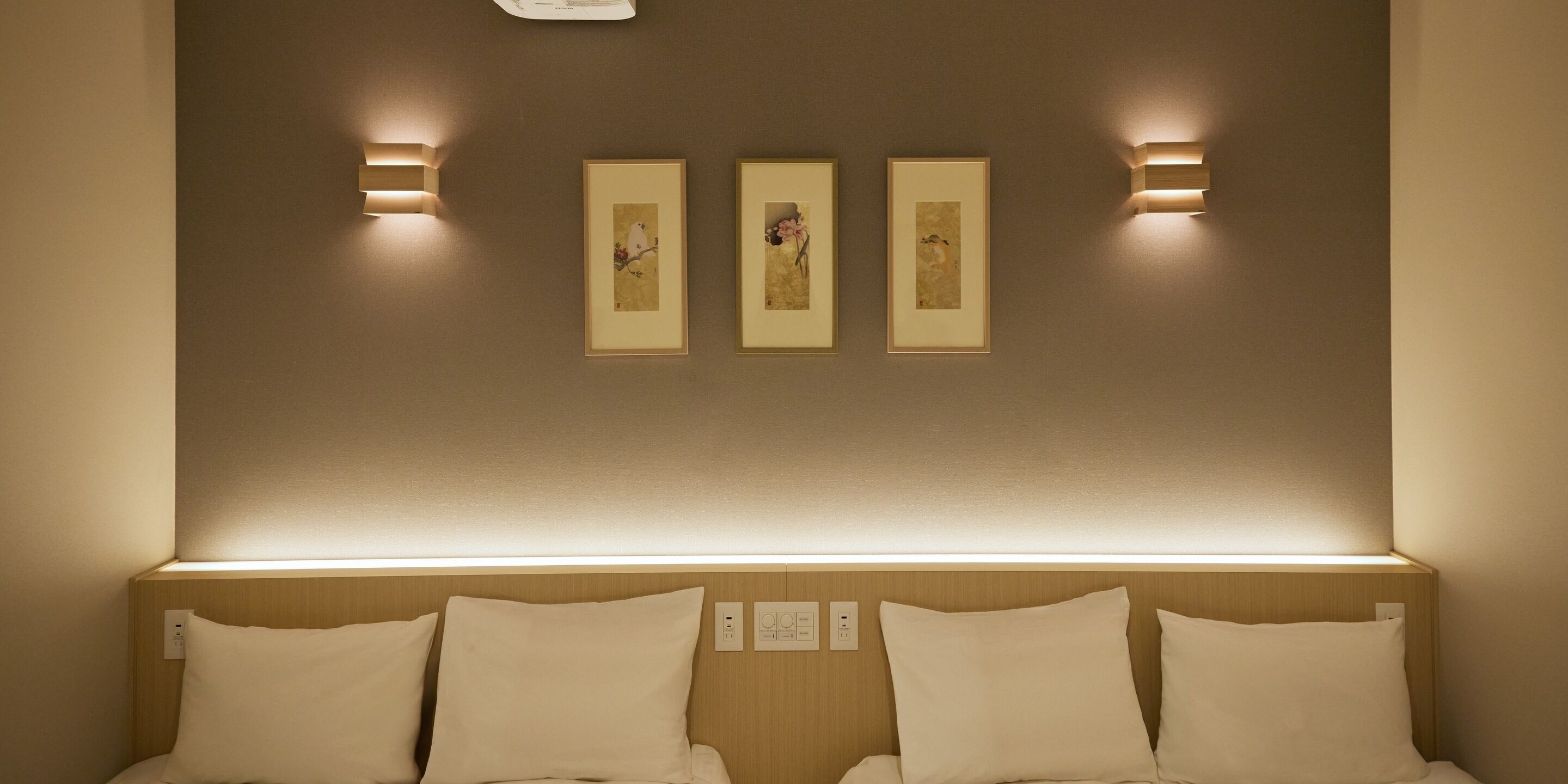 A hotel room with a bed, a headboard, and three framed artworks on the wall.