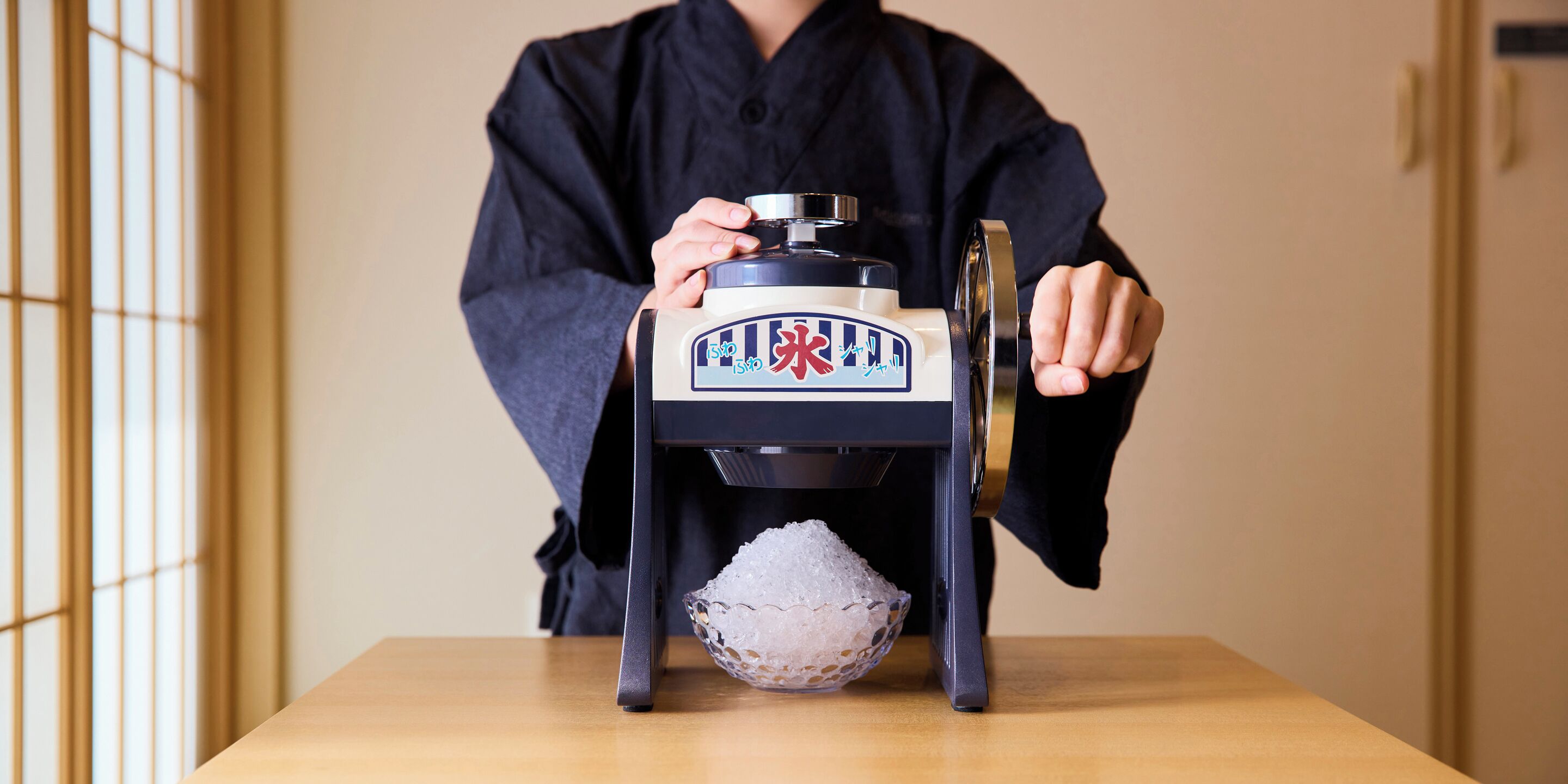 Una persona vestida de negro operando una máquina tradicional japonesa para hacer hielo.