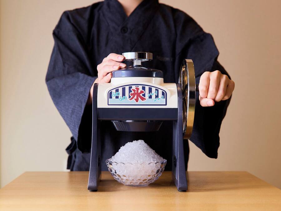 Una persona vestida de negro operando una máquina tradicional japonesa para hacer hielo.