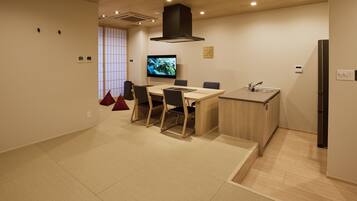A modern kitchen with a dining area, wooden flooring, and a large TV screen.