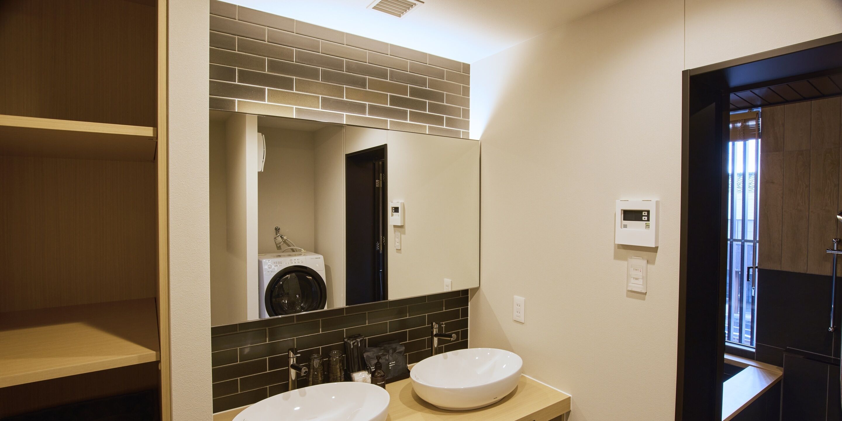 A modern bathroom with two sinks, a mirror, a washing machine, and a shower area.