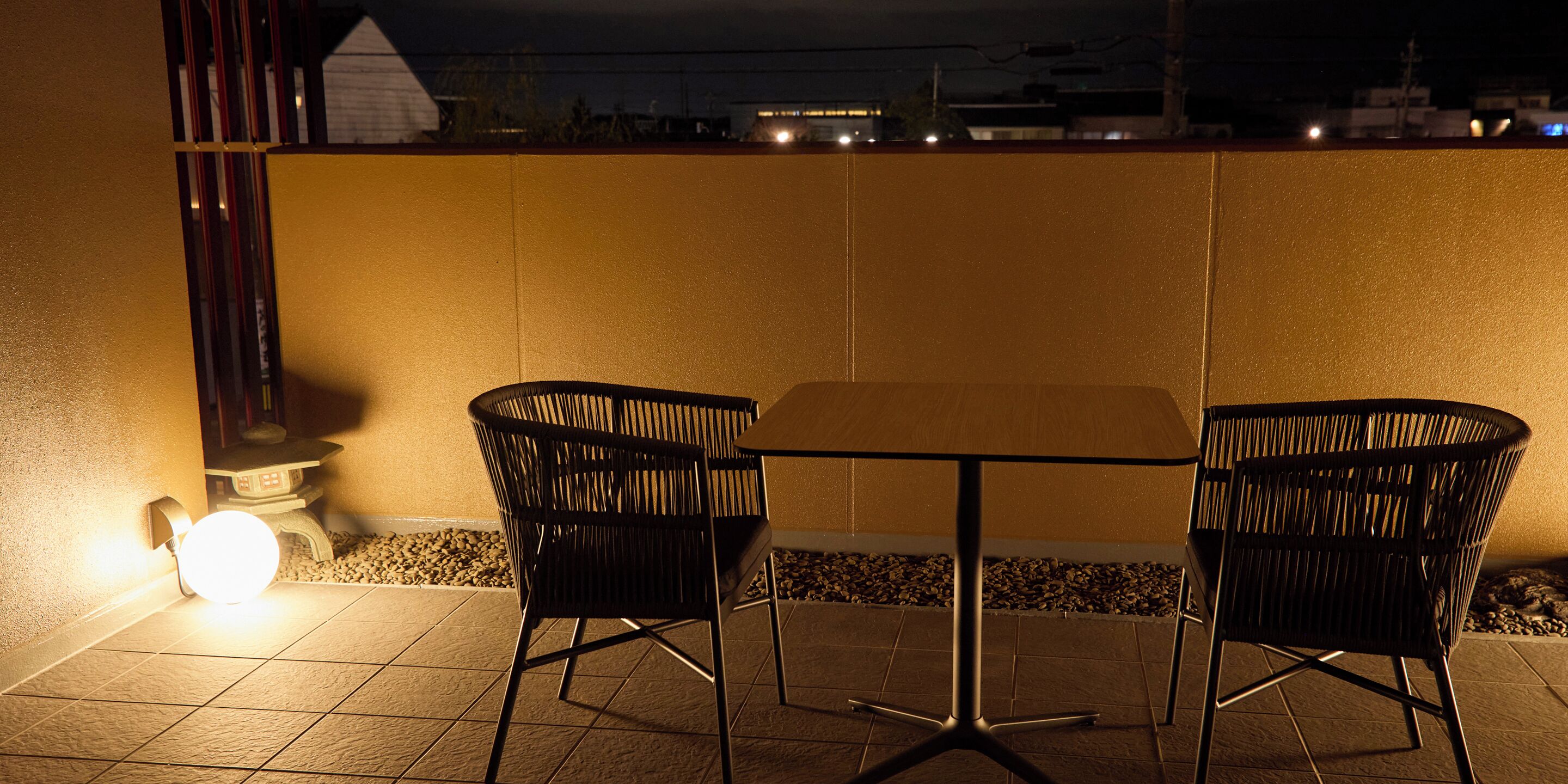 A patio with two chairs and a table, a wall, and a light source.