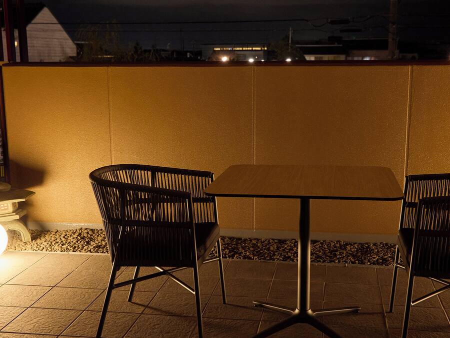 A patio with two chairs and a table, a wall, and a light source.
