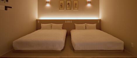 Une chambre d’hôtel avec deux lits simples, une tête de lit en bois, des appliques murales et des œuvres d’art encadrées au-dessus des lits.