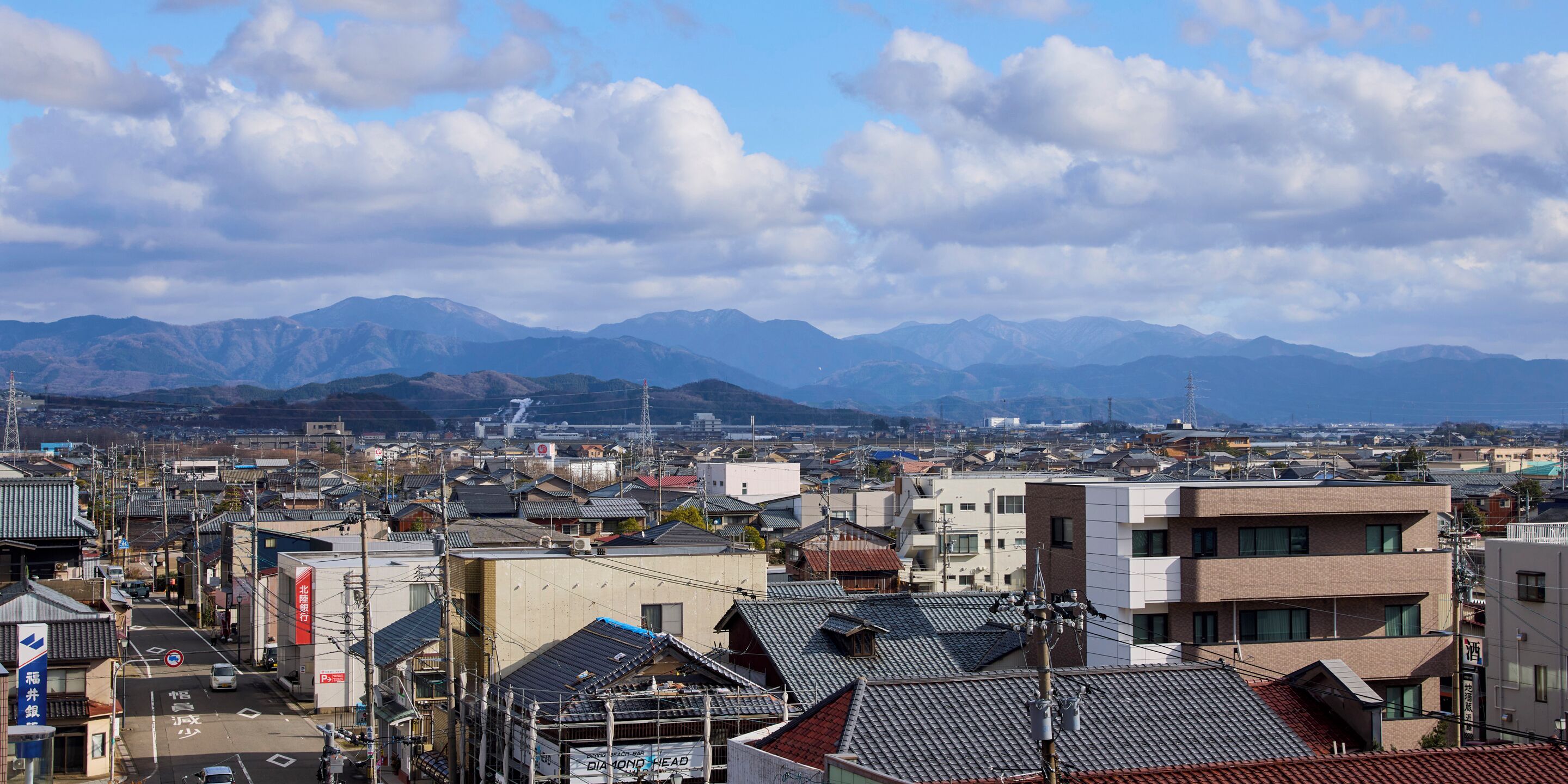 A cityscape with traditional and modern buildings, a clear sky, and mountains in the background.