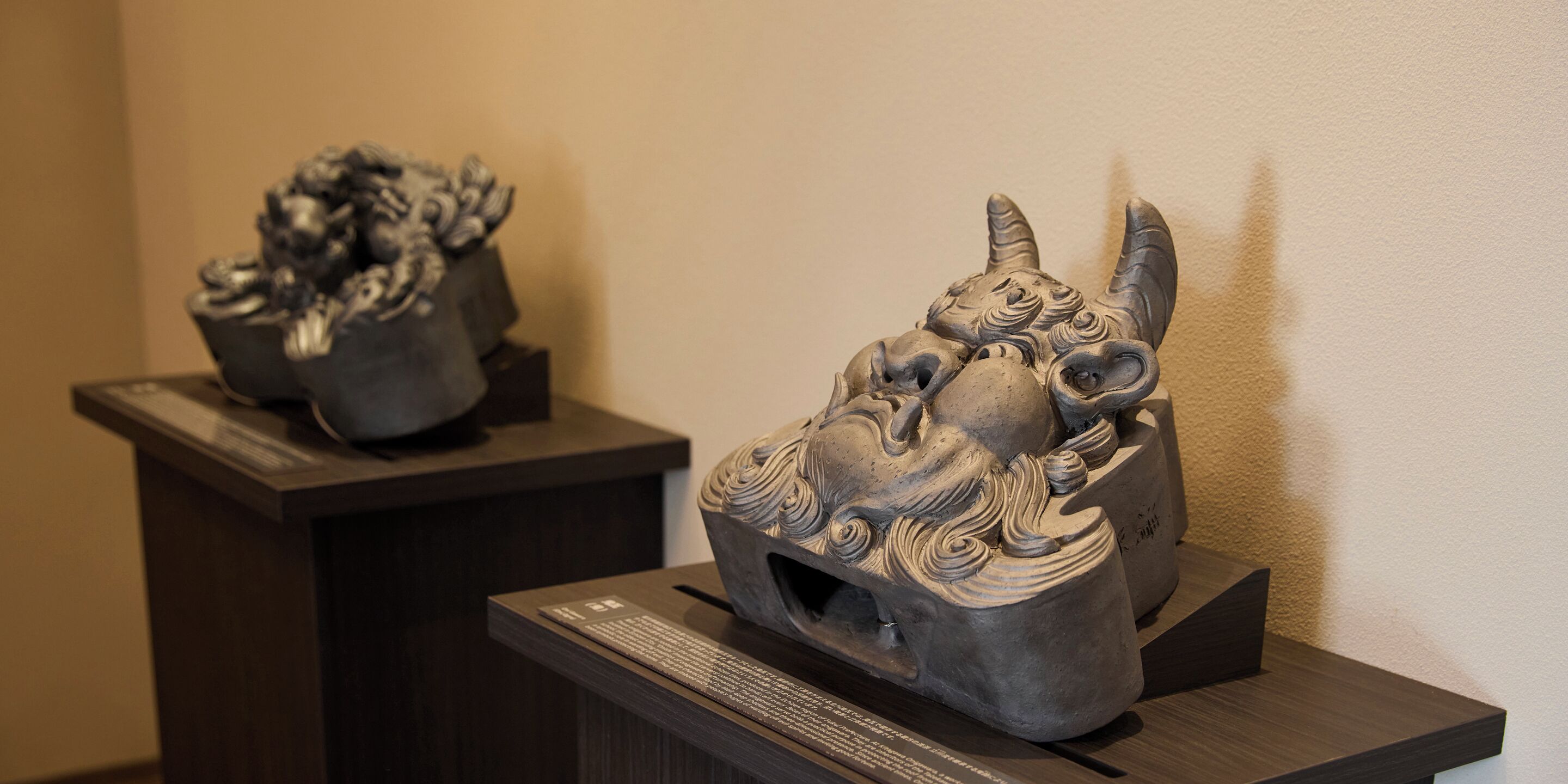 Two sculptures on dark pedestals against a plain wall.