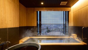 A modern bathroom with a large bathtub, a window with vertical blinds, and a visible cityscape outside. - Rakuten STAY Awara Onsen (Awara)