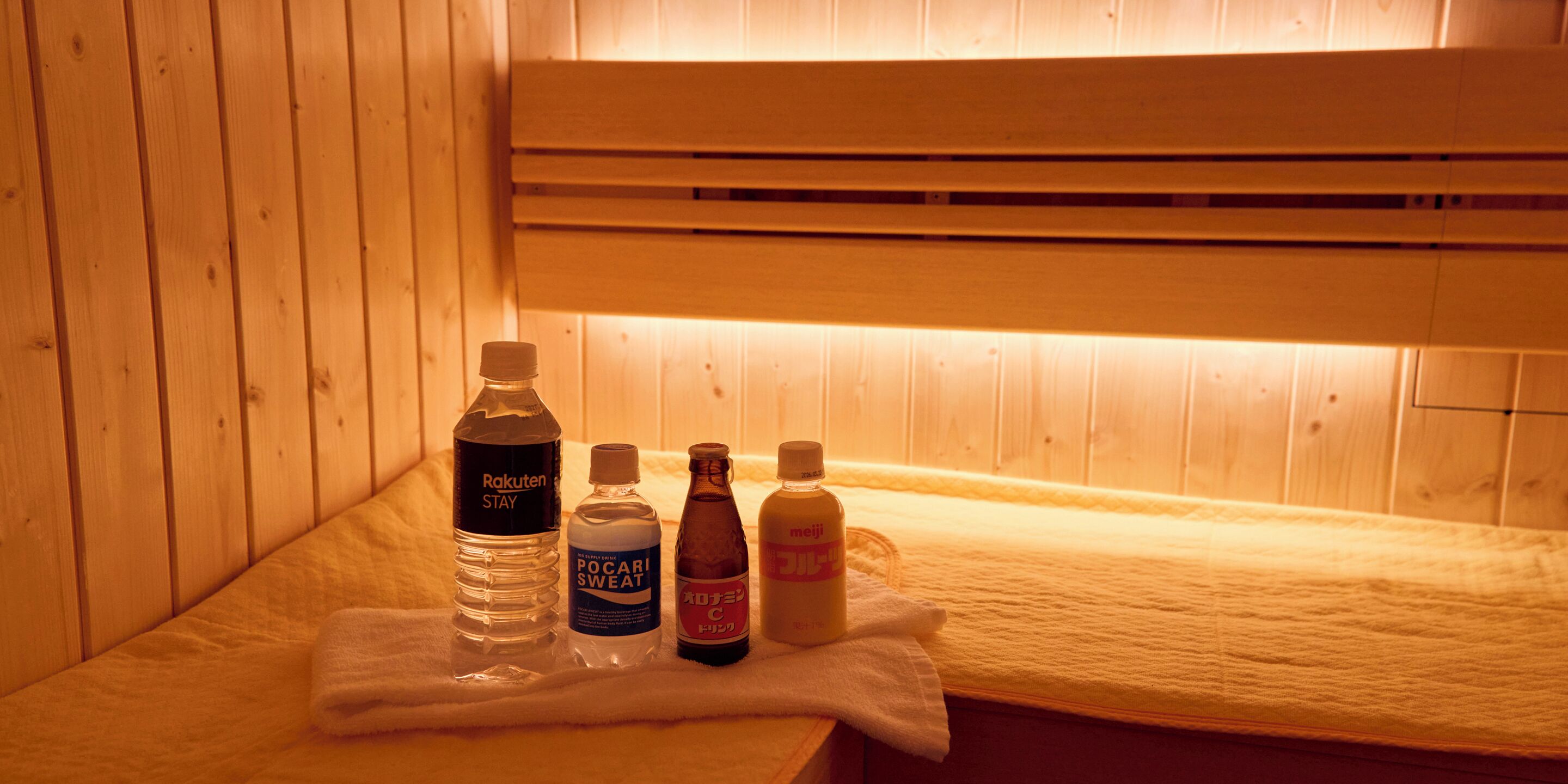 A wooden sauna with a bench, a towel, and bottles of water and lotions.