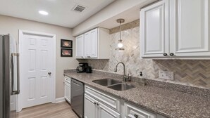 A kitchen with white cabinets, granite countertops, a stainless steel sink, and a dishwasher. - Pet-Friendly St. Simons Island Condo | Pool, Pickleball & East Beach Access (Saint Simons Island)