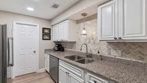 A kitchen with white cabinets, granite countertops, a stainless steel sink, and a dishwasher.