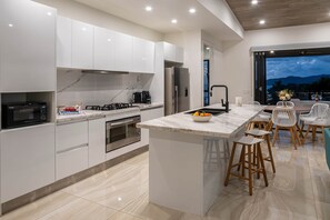 A modern kitchen with white cabinetry, a central island with bar stools, and a view of the outdoors. - Hidden Cove 17 (Hamilton Island)