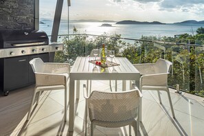 An outdoor dining area with a table and chairs, a grill, and a view of the sea. - Hidden Cove 17 (Hamilton Island)