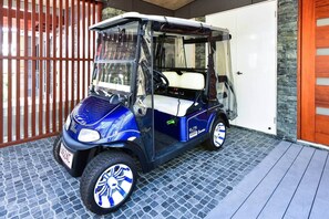 Ein kleiner, blau-weißer Golfwagen auf einem Kopfsteinpflasterparkplatz.