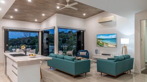 A modern living space with a kitchen island, seating area, and large windows offering views of the outdoors. - Hidden Cove 17 (Hamilton Island)