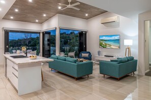 Ein modernes Wohnzimmer mit Kücheninsel, Sitzgelegenheit und großen Fenstern mit Blick ins Freie.