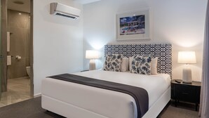 A modern hotel room with a large bed, two bedside lamps, a headboard with a geometric pattern, and a framed picture on the wall. - Hidden Cove 17 (Hamilton Island)