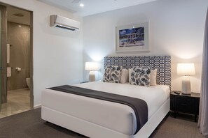 Ein modernes Hotelzimmer mit einem großen Bett, zwei Nachttischlampen, einem geometrisch gemusterten Kopfteil und einem gerahmten Bild an der Wand.