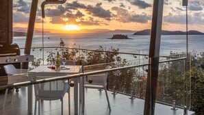 A balcony with a table set for two, overlooking a sunset over the sea with a ship in the distance. - Hidden Cove 17 (Hamilton Island)