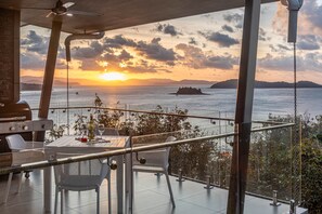 Ein Balkon mit Tisch für zwei Personen, mit Blick auf einen Sonnenuntergang über dem Meer, ein Schiff ist in der Ferne zu sehen.