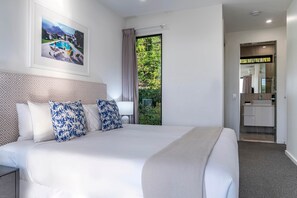 A hotel room with a large bed, a bathroom with a mirror and sink, and a view of greenery outside. - Hidden Cove 17 (Hamilton Island)