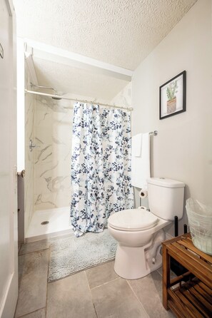 A bathroom with a shower, toilet, and a small wooden table. - Spacious Duplex for 14 in Downtown (Indianapolis)