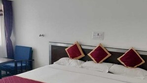 A hotel room with a large bed, a ceiling fan, a chair, and a window with curtains. - Hotel Palika (Hassan)