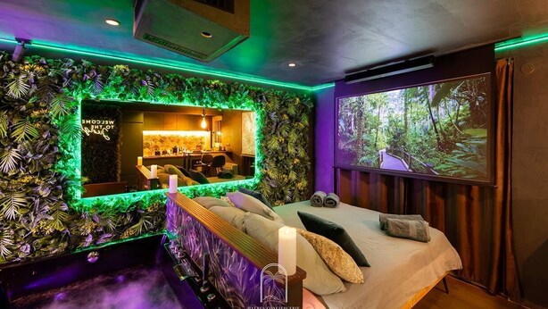 Una stanza con un letto, uno specchio, una TV e una parete decorata con piante.