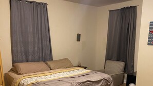 A bedroom with a bed, a chair, a nightstand, and a wall-mounted light fixture.