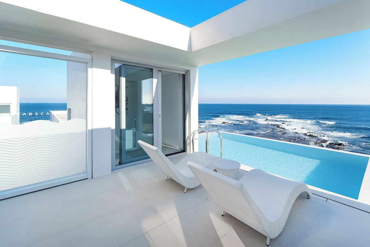 A balcony with a view of the ocean, white wicker furniture, and a glass door leading to a room.