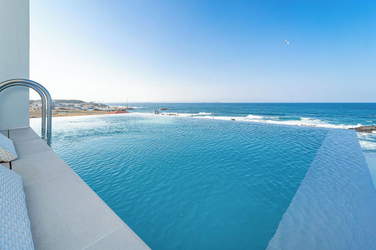 An infinity pool with a clear view of the ocean and a rocky shoreline.