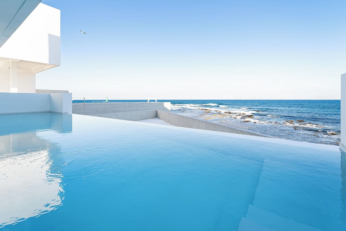 A modern infinity pool with a clear view of the sea and rocky shoreline.