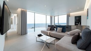 En moderne stue med stort vindue der giver udsigt over havet, en sofa, et sofabord og et fladskærms-tv.