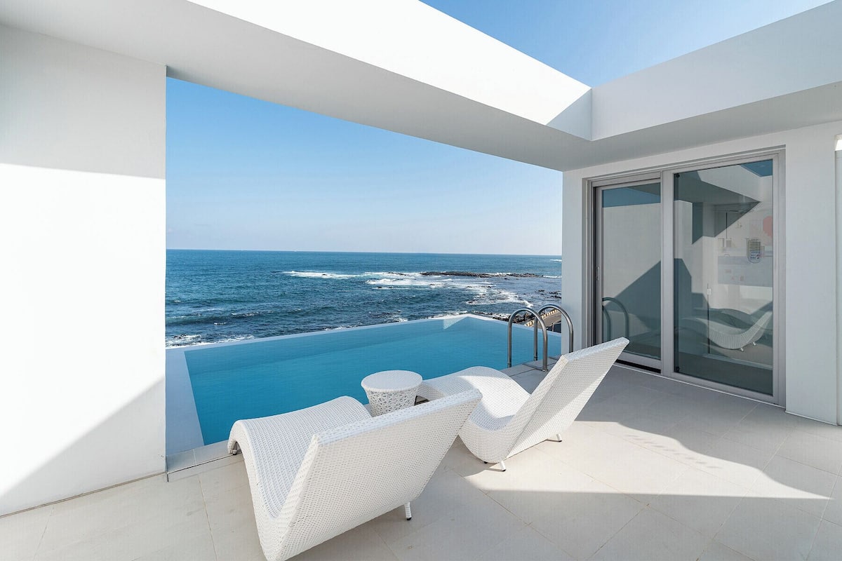 A modern balcony with a glass door leading to a pool overlooking the ocean.