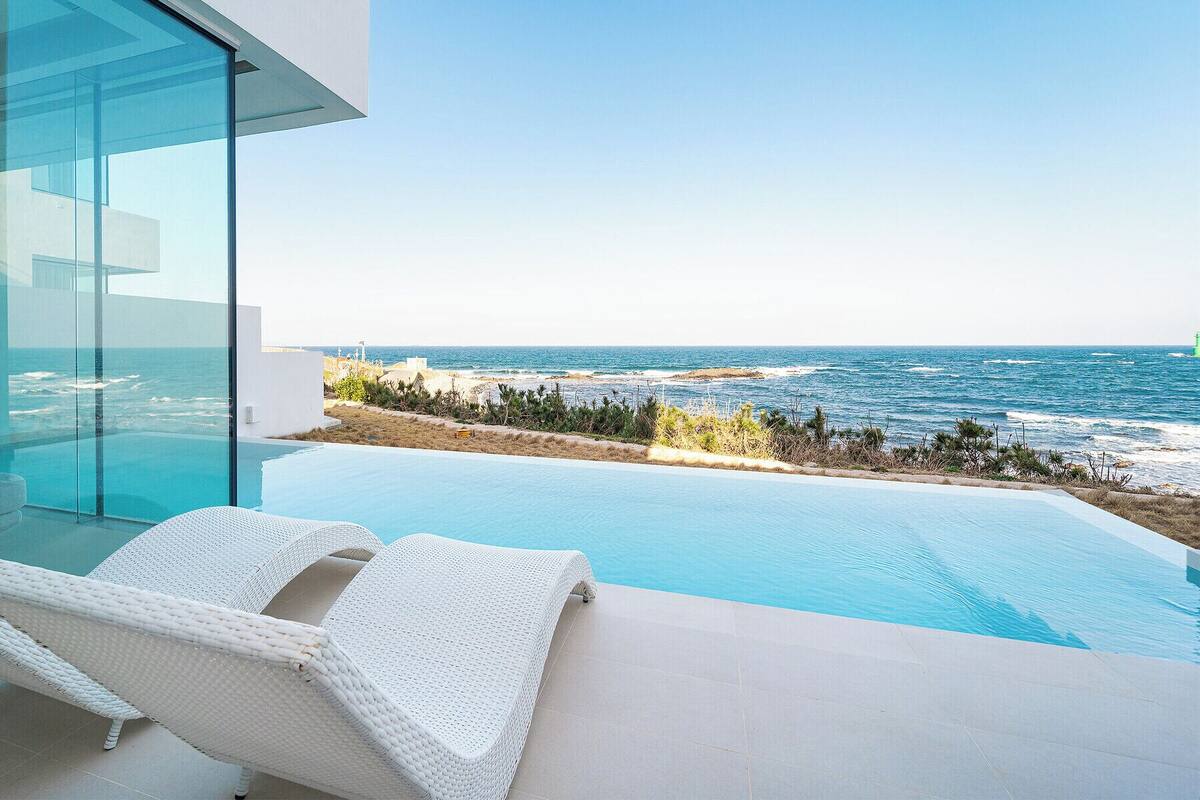 A modern infinity pool with a clear view of the ocean and a beach.