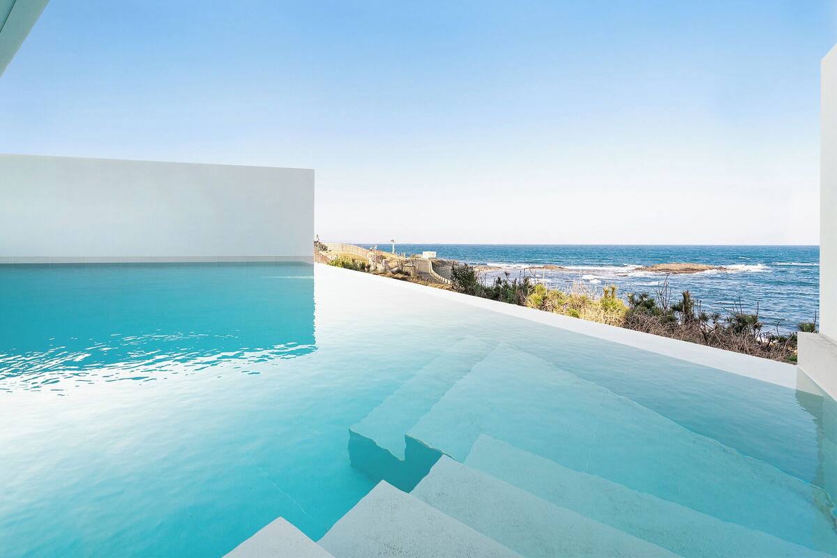 A modern infinity pool with a clear view of the ocean and rocky coastline.