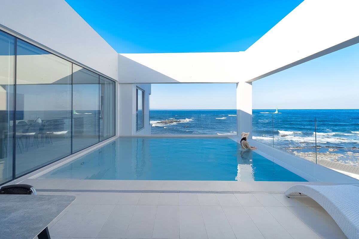 A modern infinity pool with a view of the ocean and a lighthouse.