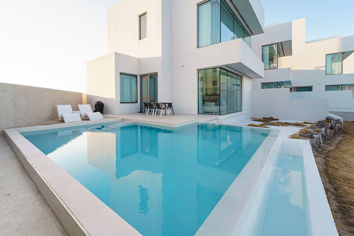 A modern pool area with a clear pool, lounge chairs, and a dining table.