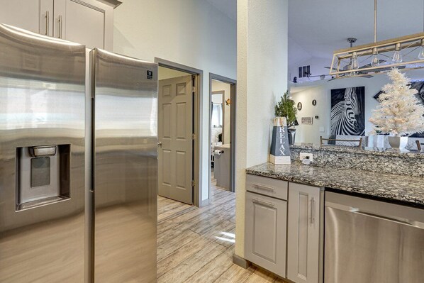 A modern kitchen with stainless steel appliances, a granite countertop, and a view into the adjacent living area. - Lake, Sxs, Deck,Hot Tub,Dock, Kayaks,Paddle Boards, Jet Ski, & or Boat Rentals (Versailles)