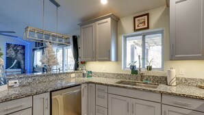 A kitchen with granite countertops, white cabinets, a dishwasher, and a window with a view.
