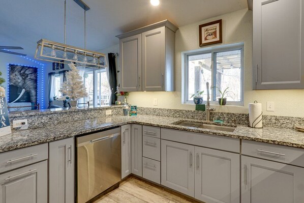 A kitchen with granite countertops, white cabinets, a dishwasher, and a window with a view.