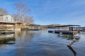A calm lake with docked boats, a covered boat house, and a house with a covered porch.
