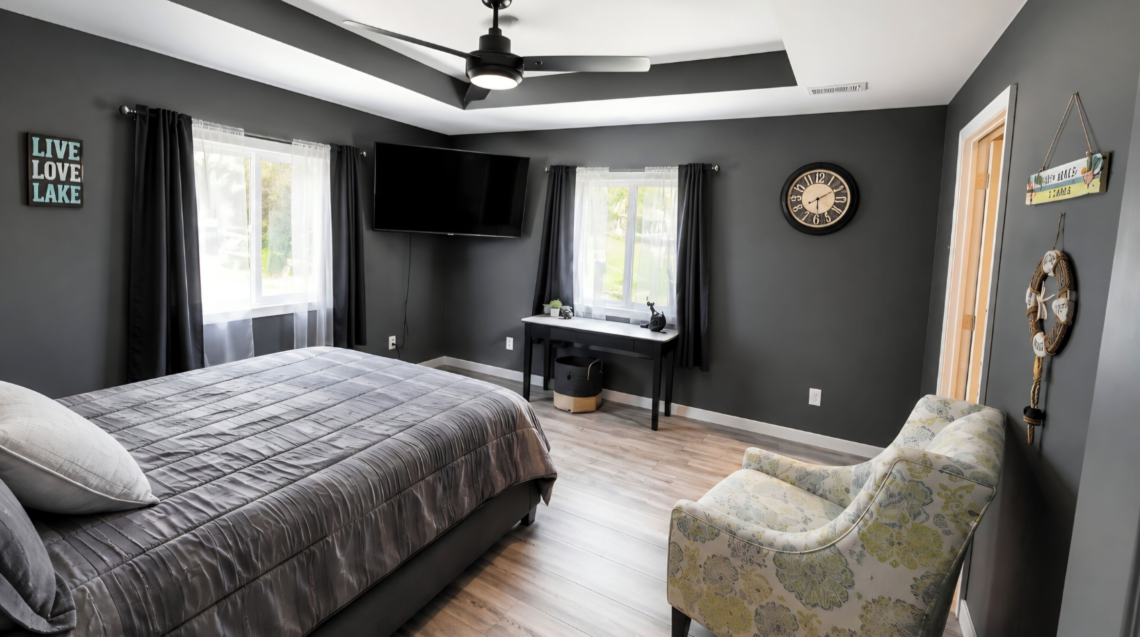Un dormitorio con cama, escritorio, silla, televisor y un reloj en la pared.