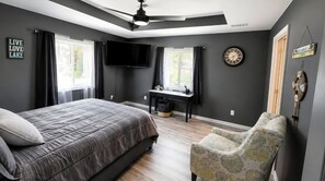 A bedroom with a bed, a desk, a chair, a TV, and a clock on the wall.