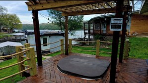 A wooden deck with a hot tub, a wooden cabin, and a view of the lake.