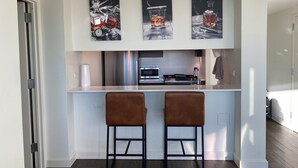 A modern kitchen with a white countertop, two brown bar stools, a stainless steel oven, and a microwave.