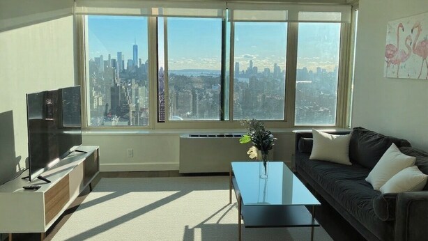 A modern living room with a large window, a flat-screen TV, a glass coffee table, and a dark-colored sofa.
