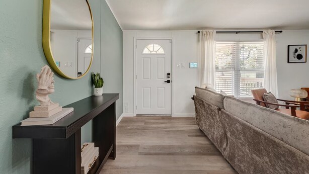 A hallway with a dark console table, a large mirror, a white door, and a seating area with a cushioned bench. - Newly Remodeled Mobile Home The Green Showcase! (Mineral Wells)