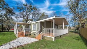 A two-story house with a covered porch, a small deck, and a gravel pathway leading to the entrance. - Newly Remodeled Mobile Home The Green Showcase! (Mineral Wells)